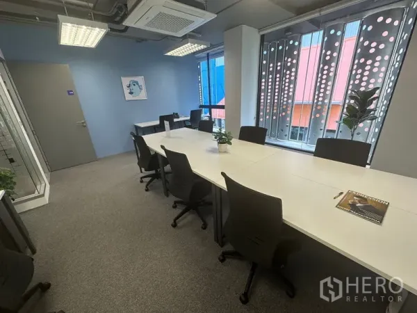 办公空间 出租 - 采光充足的办公室，长条白色办公桌与人体工学椅，大窗配打孔遮阳板，近BTS Phrom Phong站。