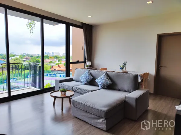 คอนโด ให้เช่าในWatthana, Bangkok - ห้องนั่งเล่นสว่างพร้อมกระจกเต็มผนัง ระเบียง และวิวเมืองสีเขียวมองเห็นคอร์ตเทนนิส