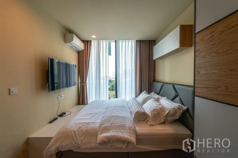 Condominium for rent in Watthana, Bangkok - Bright bedroom with floor-to-ceiling windows, wall-mounted TV and padded headboard.