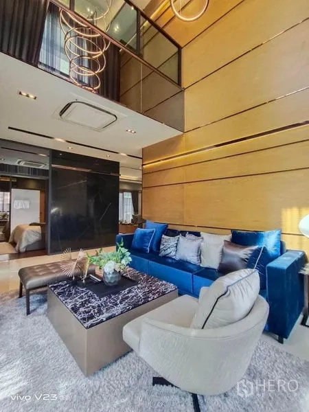 Detached House for sale in Wang Thonglang, Bangkok - Double-height living room with blue velvet sofa, marble coffee table and statement chandelier.