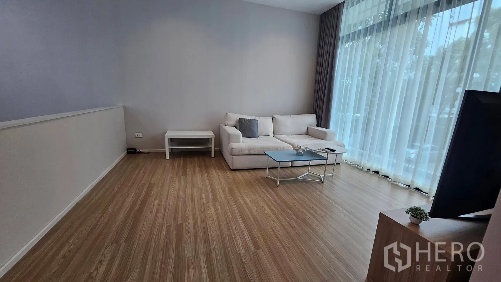 Townhouse for rent in Saphan Sung, Bangkok - Living room with sofa, coffee table, TV console, and wide sheer-curtain glazing.
