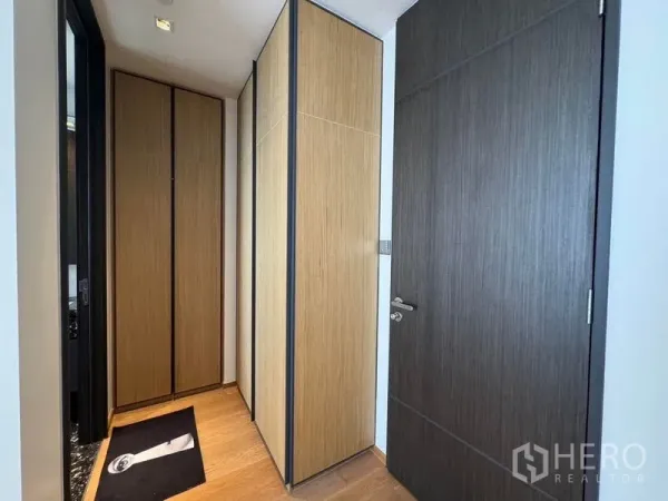 คอนโด ให้เช่า - โถงทางเข้าพร้อมตู้เสื้อผ้าบิวท์อินลายไม้และประตูสีเข้ม