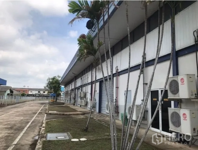 工厂 出租在Bang Bua Thong, Nonthaburi - 厂房侧面有棕榈树、空调外机与维修通道。