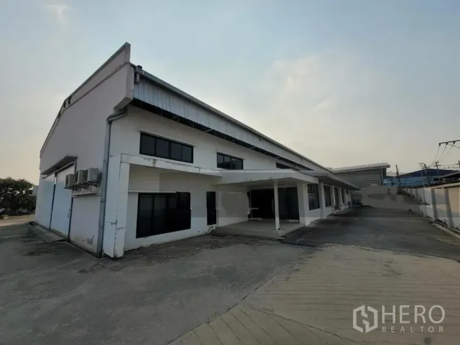 工厂 出租或出售在Prawet, Bangkok - 白色工厂建筑正面，带有雨棚入口和宽阔车道。