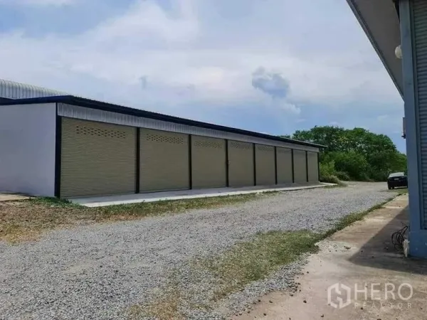 货栈 出租在Chon Buri - 一排卷闸储物间，旁有碎石车道与停车区域。