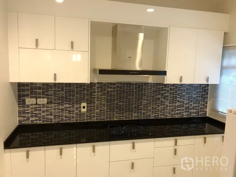 Detached House for rent or sale in Saphan Sung, Bangkok - Modern kitchen with white cabinetry, black stone countertop and mosaic tile backsplash with range hood.