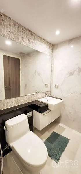 Condominium for rent - Contemporary bathroom with marble-look walls, large mirror, vanity sink and toilet.