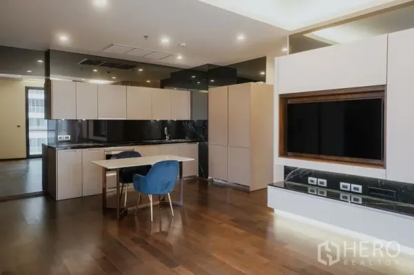 Condominium for rent or sale in Watthana, Bangkok - Open‑plan kitchen with beige cabinets, black backsplash, dining table and TV feature wall.