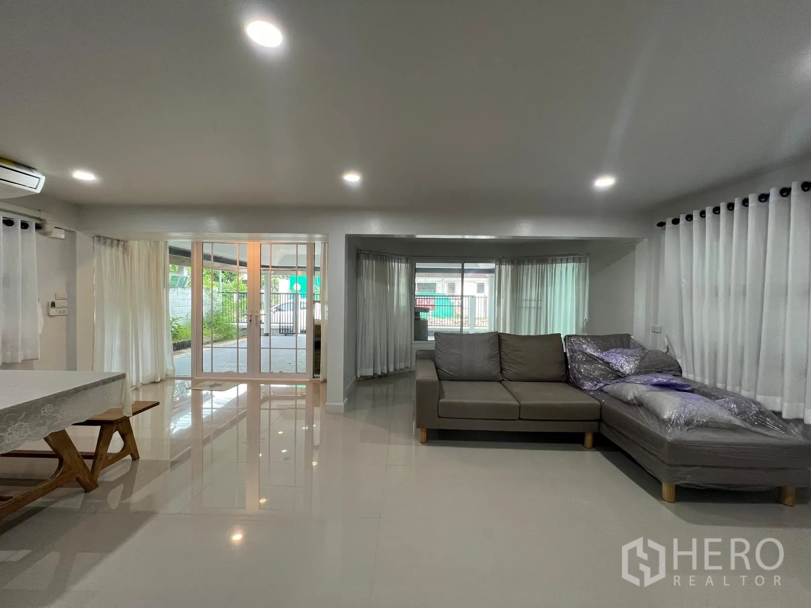 Detached House for rent in Saphan Sung, Bangkok - Open-plan living and dining area with L-shaped sofa, glossy tile floors and sliding doors to the patio.
