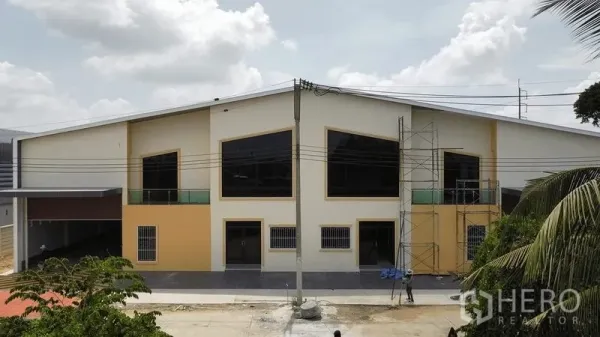 Warehouse for rent in Bang Pakong, Chachoengsao - Modern warehouse exterior with large black-framed windows, scaffolding and a wide driveway.