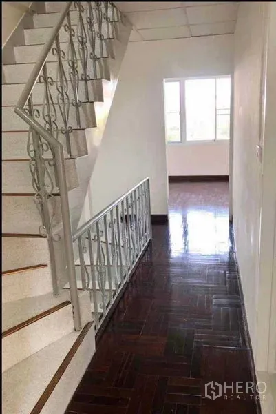 Home Office for rent or sale in Watthana, Bangkok - Internal staircase with decorative metal railing beside a corridor leading to a bright room.
