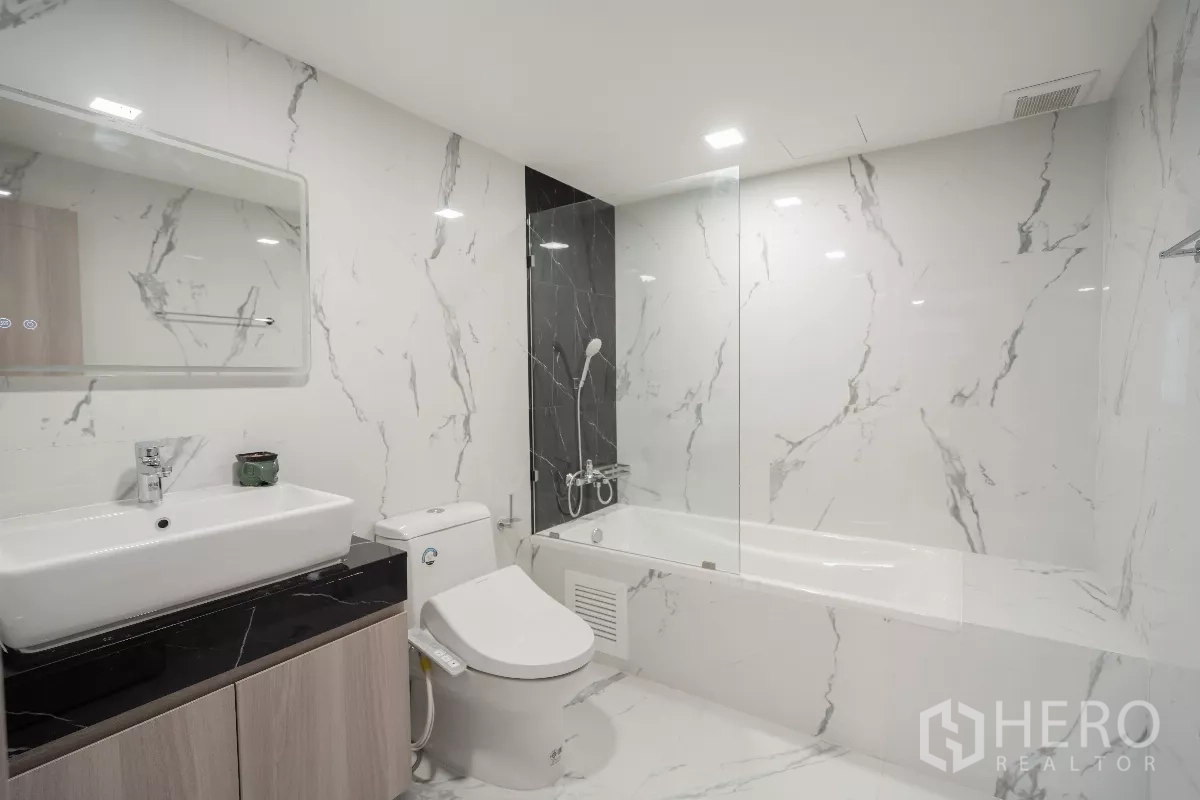 Apartment for rent - Marble-tiled bathroom with bathtub, glass shower screen, modern vanity and toilet.