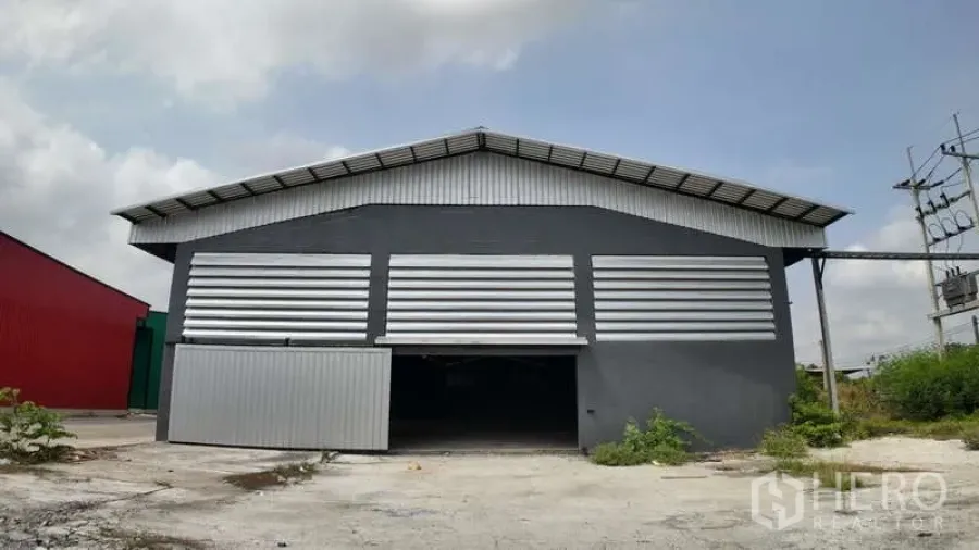 Warehouse for rent in Chachoengsao - Front elevation of a grey steel‑clad warehouse with louvered panels, large sliding door and concrete yard.