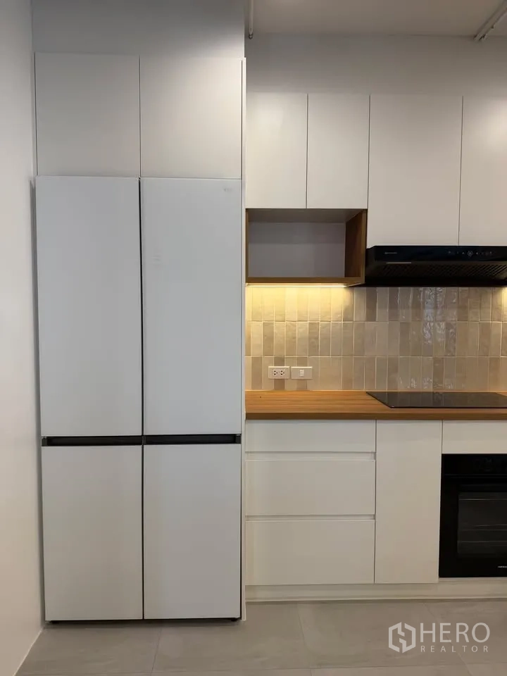Condominium for rent in Watthana, Bangkok - Tall refrigerator beside cabinetry, cooktop, and built-in oven.