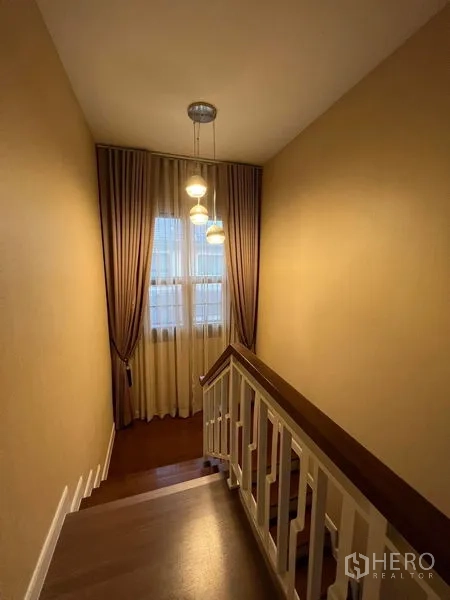 Detached House for rent or sale in Bang Phli, Samut Prakan - Wood staircase with white railing and pendant lighting by a tall window.