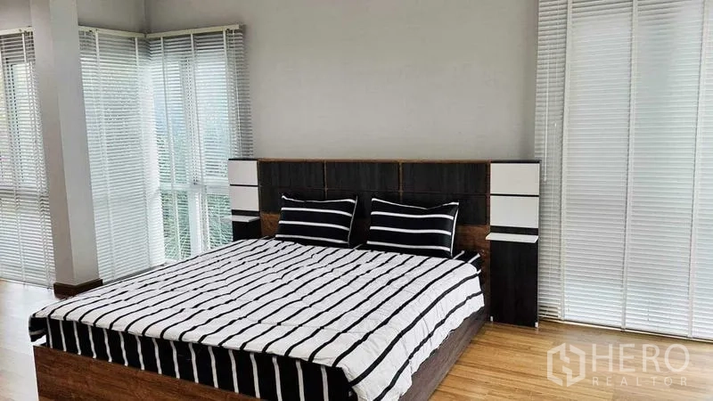 บ้าน ให้เช่าในLam Luk Ka, Pathum Thani - ห้องนอนรับแสงดี พื้นไม้ เตียงลายทาง และกระจกมุมพร้อมมู่ลี่