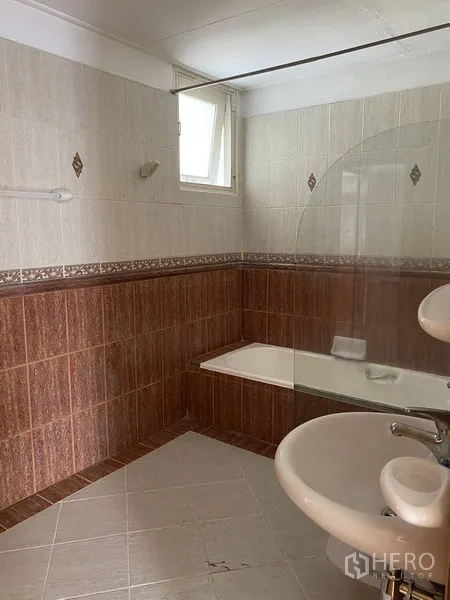 Apartment for rent in Khlong Toei, Bangkok - Tiled bathroom with bathtub, glass screen, sink and small window for ventilation.