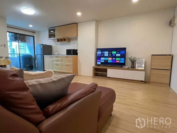 Condominium for rent in Ratchathewi, Bangkok - Living space with leather sofa facing smart TV, minimalist kitchen, and access to a balcony.