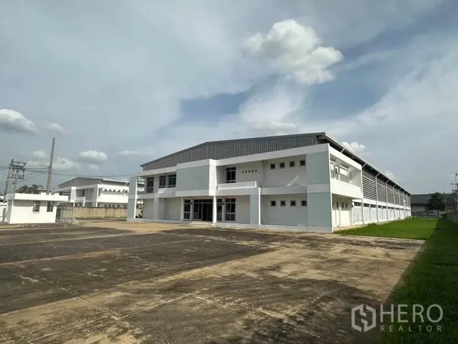 工厂 出租在Phra Nakhon Si Ayutthaya - 邦巴茵现代白色工厂，金属屋顶与宽阔硬化装卸场，天空晴朗。