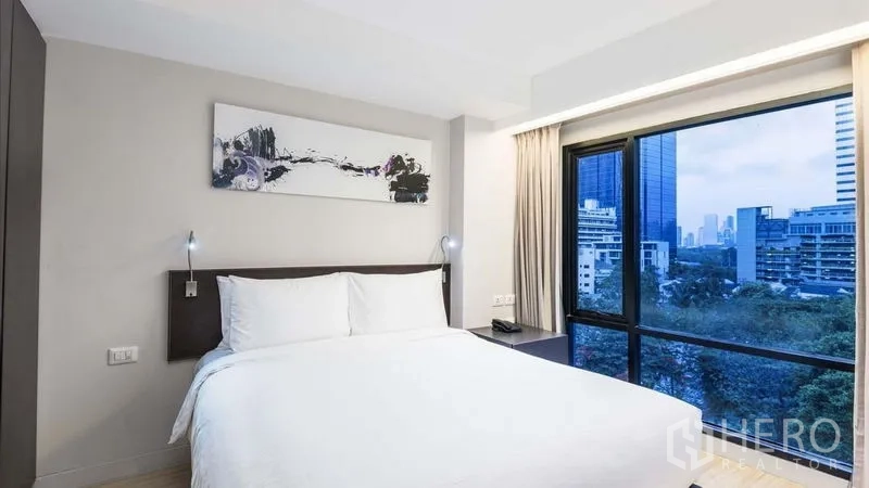 Apartment for rent in Watthana, Bangkok - Second bedroom with corner windows overlooking greenery and city buildings.