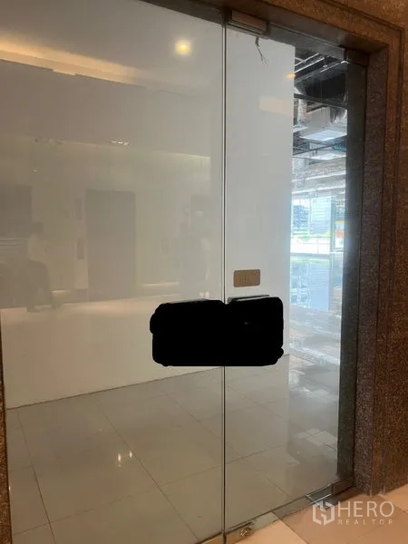 零售空间 出租 - 无框玻璃入户门，金属把手与明亮的室内。