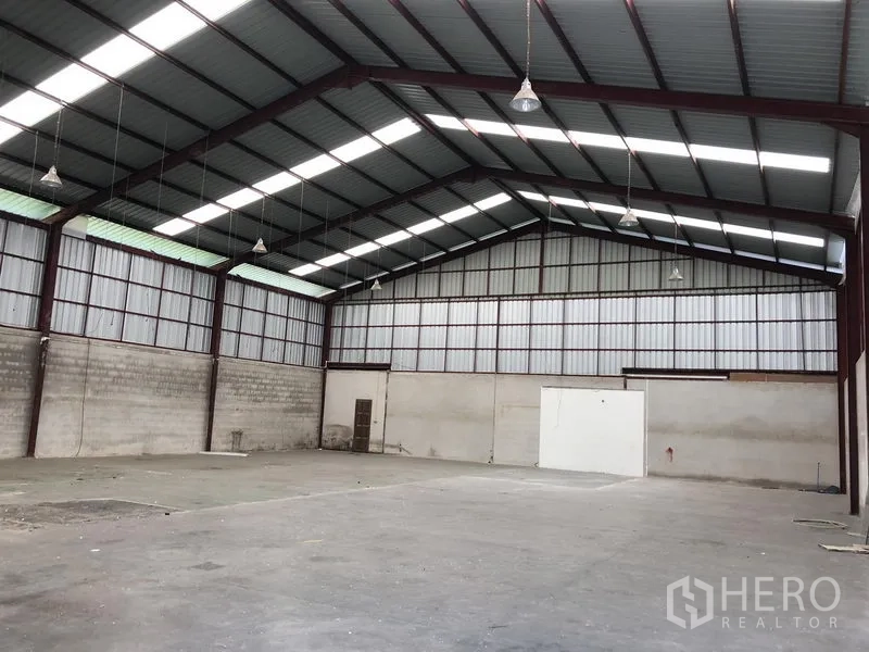คลังสินค้า ให้เช่าในBueng Kum, Bangkok - ภายในโกดังโล่งกว้าง เพดานโครงเหล็กสูง มีช่องแสงและพื้นคอนกรีตพร้อมโคมไฟแขวน.