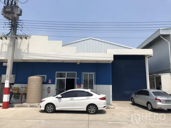 工厂 出租在Khlong Luang, Pathum Thani - 工业园内蓝色厂房外立面，卷帘门与停车位