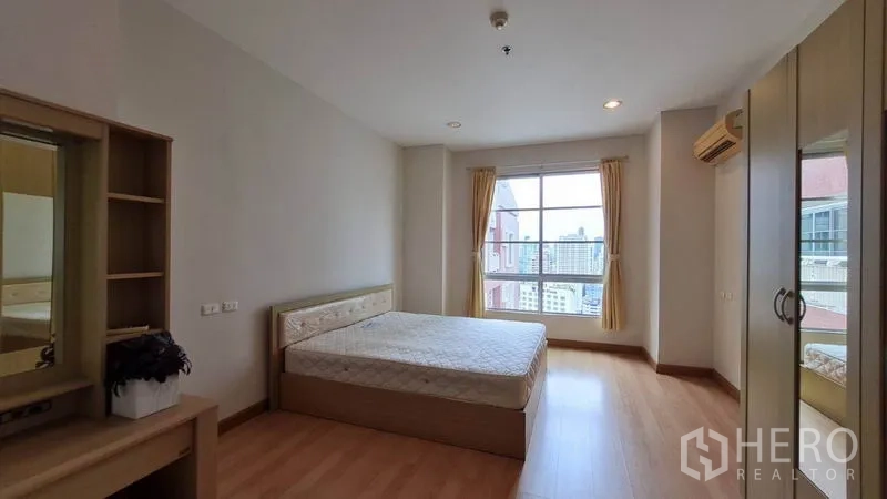 Condominium for rent in Khlong Toei, Bangkok - Spacious third bedroom with large window, bed, wardrobe, and wooden flooring.