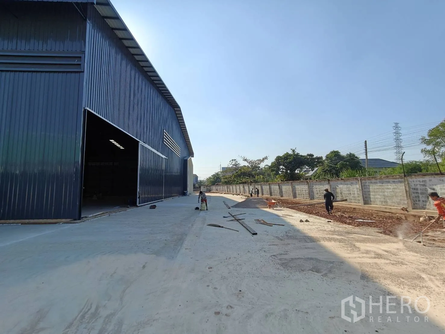 Factory for rent in Mueang Samut Sakhon, Samut Sakhon - Large metal-clad factory with wide sliding door and long concrete driveway beside a boundary wall.