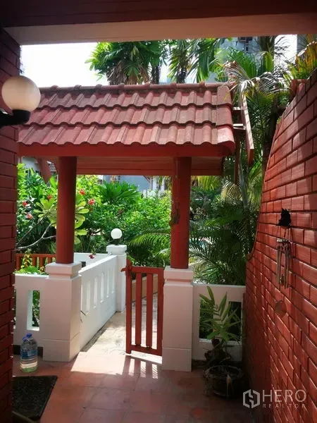 Townhouse for rent or sale in Watthana, Bangkok - Townhouse entry with red tiled roof, brick walls and a lush tropical garden.