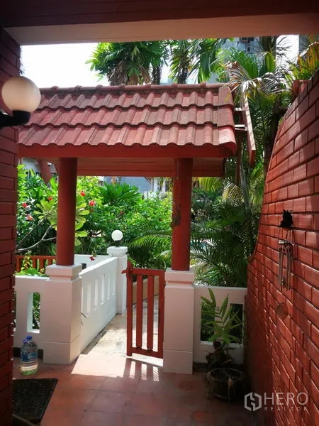 Townhouse for rent or sale in Watthana, Bangkok - Townhouse entry with red tiled roof, brick walls and a lush tropical garden.