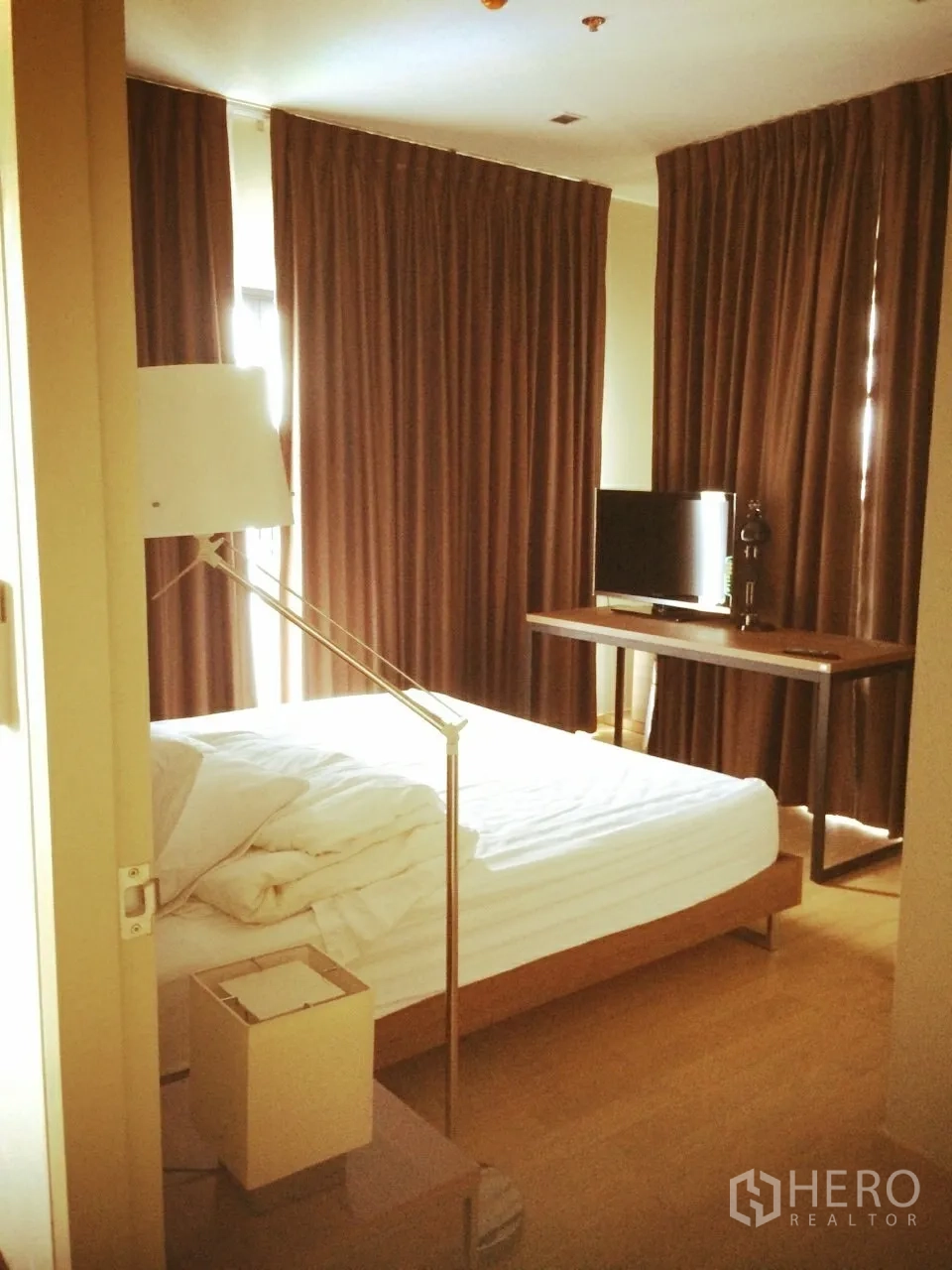 Condominium for rent or sale in Watthana, Bangkok - Bright bedroom with bed, floor lamp and TV by the window with heavy curtains.