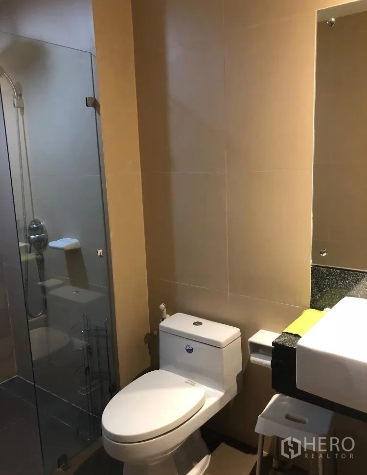 公寓 出租在Watthana, Bangkok - 浴室内设马桶、台盆、大镜与相邻的玻璃淋浴房。