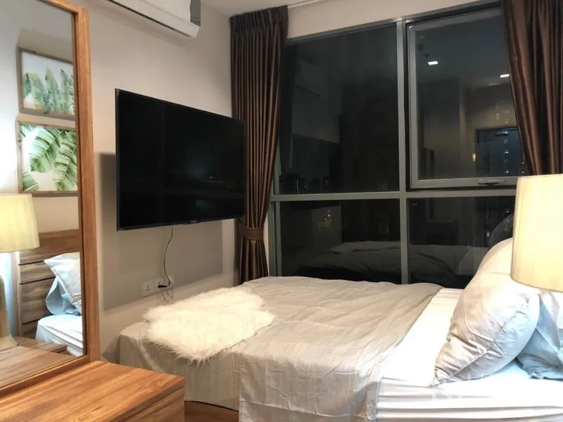 Condominium for rent or sale in Phra Khanong, Bangkok - Primary bedroom with large window, wall-mounted TV and neutral bedding.