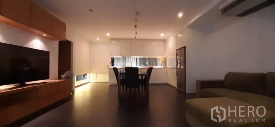 คอนโด ให้เช่าในPhaya Thai, Bangkok - ห้องนั่งเล่นแบบโอเพ่นสเปซ มีโซฟา ชุดทีวี และครัวโทนขาวด้านหลังพร้อมไฟดาวน์ไลท์