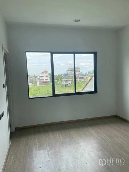 Townhouse for sale in Bueng Kum, Bangkok - Bright bedroom with a large window overlooking greenery and low-rise buildings.