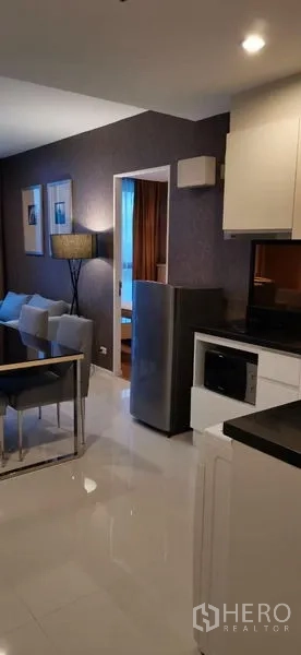 公寓 出租在Watthana, Bangkok - 紧凑厨房，设冰箱、微波炉与黑色台面，毗邻客厅。