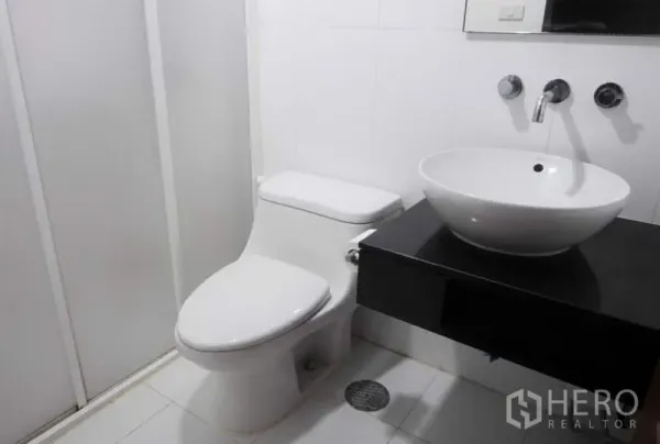 Condominium for rent in Pathum Wan, Bangkok - Modern white bathroom featuring a vessel sink, wall-mounted faucet, toilet and shower enclosure.