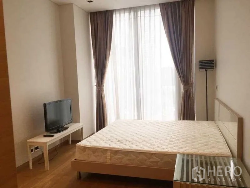 Condominium for rent in Bang Rak, Bangkok - Bedroom with double bed, TV stand, and tall window draped with curtains.