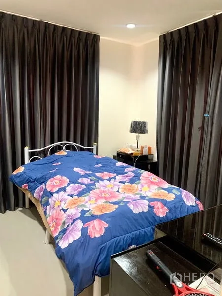 Detached House for rent in Khlong Sam Wa, Bangkok - Cozy bedroom with floral bedding, dark blackout curtains, and bedside lamp.