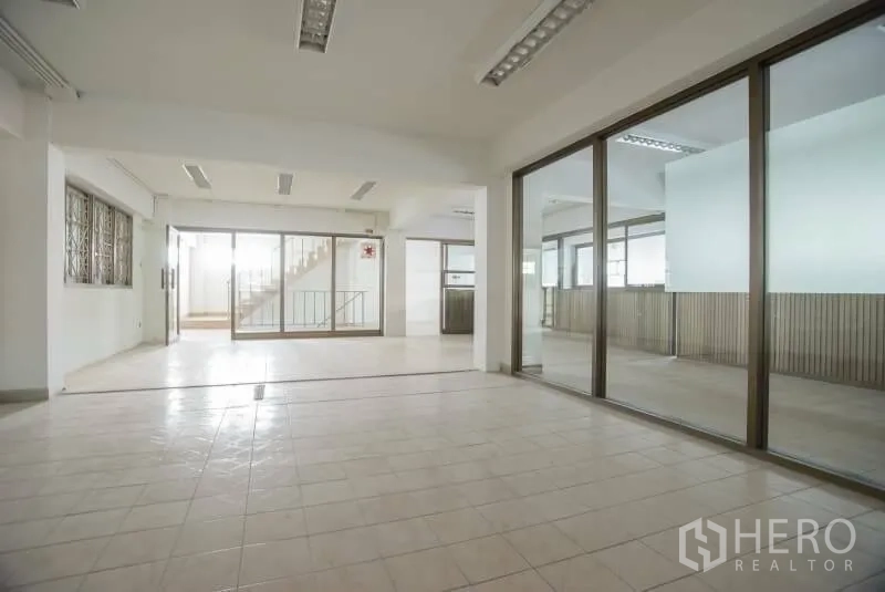 店屋 出租在Wang Thonglang, Bangkok - 一层开放式空间，瓷砖地面，玻璃隔间，后方有通往楼上的楼梯。