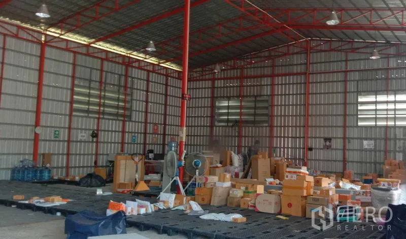 货栈 出租在Khlong Sam Wa, Bangkok - 仓库内部红色钢结构，高挑屋顶、通风百叶与照明，地面摆放货箱托盘。