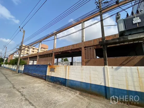 โรงงาน ขายในBang Phli, Samut Prakan - แนวกำแพงด้านนอกและโครงสร้างอาคารโรงงานติดถนน พร้อมสายไฟฟ้า
