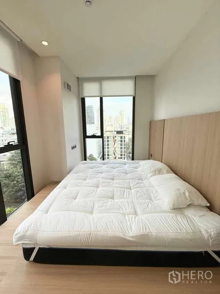 Condominium for rent in Watthana, Bangkok - Corner master bedroom with large windows, wood floors, and skyline views.