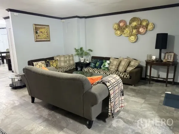 联排别墅 出租在Prawet, Bangkok - 转角起居区，L形沙发、墙面装饰与灰色地砖。