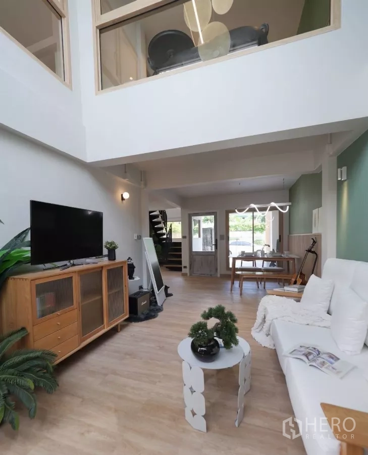 ทาวน์เฮาส์ ให้เช่าในWatthana, Bangkok - ห้องนั่งเล่นเพดานสูง มีโซฟา ตู้ทีวี และพื้นไม้ มองไปยังส่วนทานอาหารและบันได