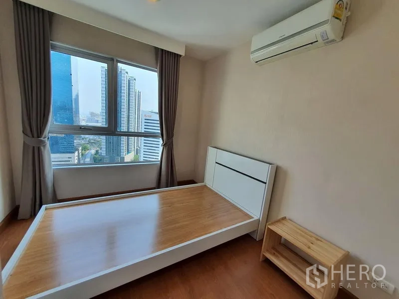 Condominium for rent in Huai Khwang, Bangkok - Second bedroom with city-view window, air conditioner and wood bedframe in Huai Khwang, Bangkok.