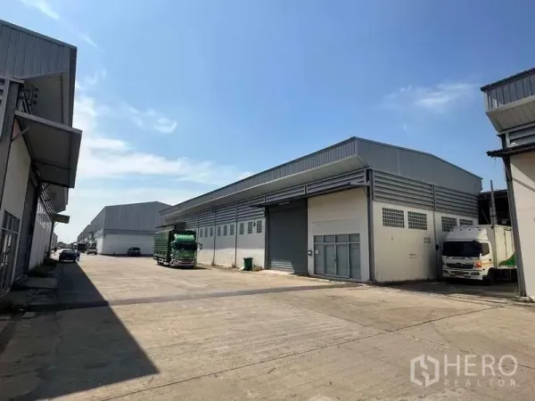 Warehouse for rent in Bang Bua Thong, Nonthaburi - Modern warehouse row with a wide concrete yard and parked trucks under a clear sky in Bang Bua Thong.