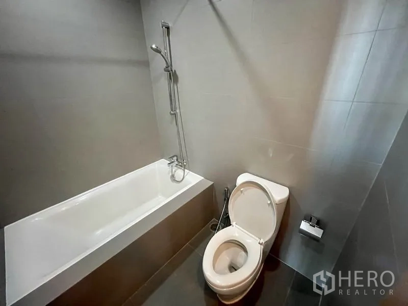 คอนโด ให้เช่าในPhaya Thai, Bangkok - ห้องน้ำสไตล์โมเดิร์นพร้อมอ่างอาบน้ำ ชาวเวอร์แบบมือถือ และโถสุขภัณฑ์ โทนกระเบื้องสีเทา.