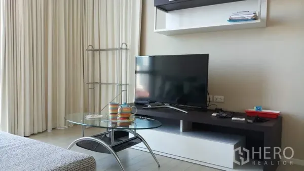 Condominium for rent in Watthana, Bangkok - Modern TV console and glass coffee table with full-length curtains in the living room.